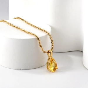 Collier chaîne corde dorée avec pendentif gemme jaune poire sur support minimaliste blanc
