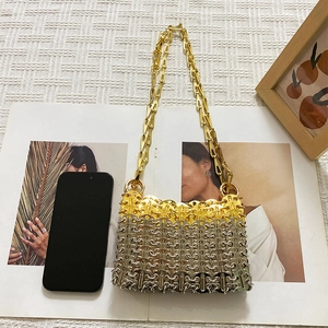 Detailed view of silver and gold metal disc chain bag next to a smartphone for size reference