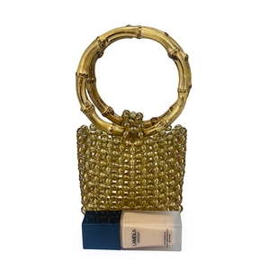 Detail view of amber beaded handbag with bamboo texture handles and reference object