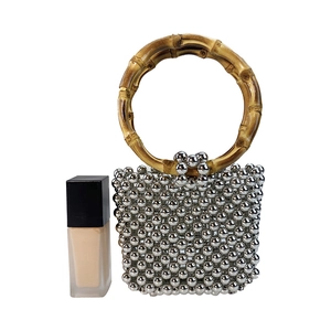 Silver beaded handbag with bamboo handle shown next to a foundation bottle for size reference