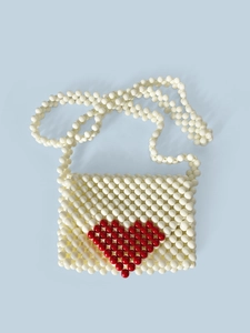 Gros plan d'un sac en perles tressées blanches avec un motif de cœur rouge sur fond bleu