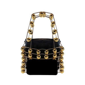 Detail of the golden hollow metal cage structure and black drawstring inner bag of the handbag