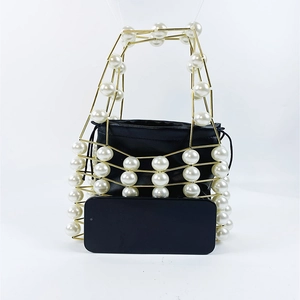 Detail view of gold hollow metal handbag with large pearls and smartphone for size scale