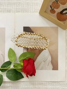 Handmade clear crystal beaded hair clip with gold accents on a magazine background