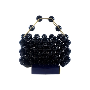 Detail of a black beaded handbag with round glossy beads and a gold metal handle