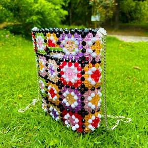 Detail of colorful handmade beaded bag with floral patterns and silver chain on green grass