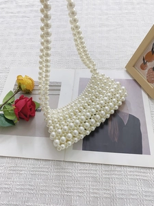 Handmade white faux pearl beaded evening bag with elegant woven handle on a white desk