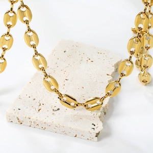 Détail du collier maille grain de café plaqué or 18K sur un socle en pierre blanche