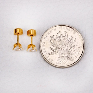 Macro shot of gold four-prong heart stud earrings with cubic zirconia next to a coin