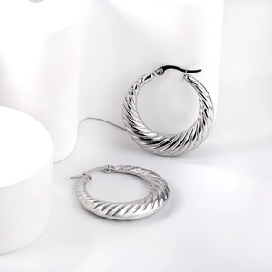 Détail macro de la texture métallique torsadée argentée des boucles d'oreilles en C