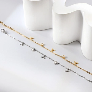 Détail de bracelets fins dorés et argentés avec zircons clairs et breloques trèfle
