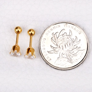 Vue macro de boucles d'oreilles en acier doré avec pierres de zircon à côté d'une pièce