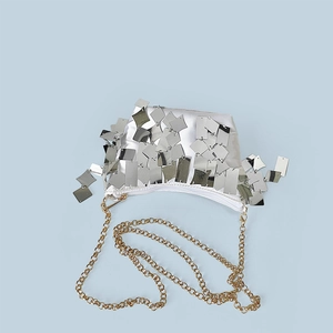 Detail of silver sequin tassel evening bag with gold chain strap on light blue background