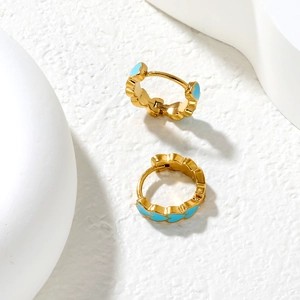 Detail of gold-plated hoop earrings with light blue enamel heart pattern on stone surface