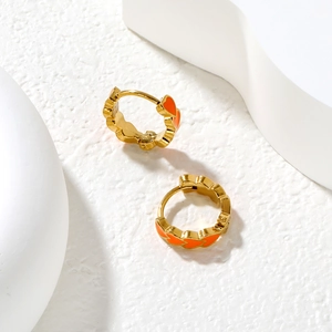 Detail of gold huggie earrings with orange enamel heart patterns on white stone