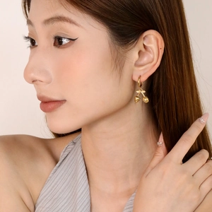 Close-up of elegant gold cherry pendant earrings with polished metallic finish on a model