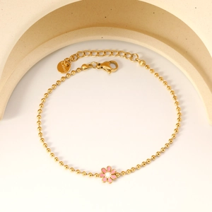 Detail of gold beaded bracelet with pink enamel flower charm and stainless steel tag