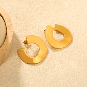Détail de boucles d'oreilles dorées géométriques creuses sur surface beige texturée