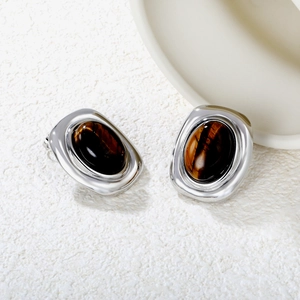Close-up of vintage oval tiger eye earrings with silver metal on white stone surface