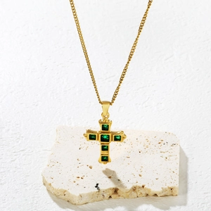 Luxurious gold cross necklace with square green gemstones on a textured stone base