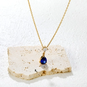 Golden necklace with clear square and blue teardrop crystal pendant on stone display
