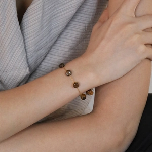 Minimalist gold chain bracelet with tiger eye beads on female wrist with grey sleeve