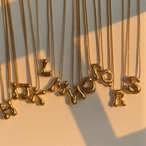 Minimalist golden bubble letter pendants with box chain on a warm beige background