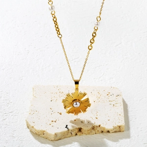 Collier doré avec pendentif perle soleil posé sur pierre beige avec ombres