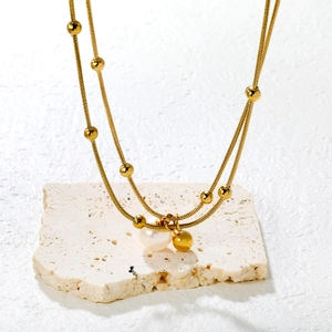 Double-layered gold pearl necklace with snake chain and round beads on white stone base