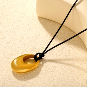 Minimalist gold teardrop pendant necklace with a black cord on a textured surface