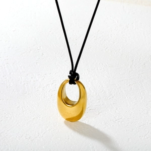 Minimalist gold oval solid pendant necklace with black cord on textured white surface