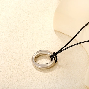 Detail of silver circular pendant with high-polish finish on minimalist black cord necklace