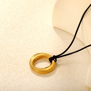 Minimalist wax cord necklace with hollow round gold pendant shown on textured surface