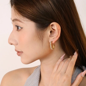 Detail of C-shaped gold-plated earring with white cubic zirconia on a model