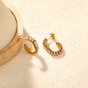 Detail of C-shaped gold-plated earrings featuring channel-set rectangular zircon stones