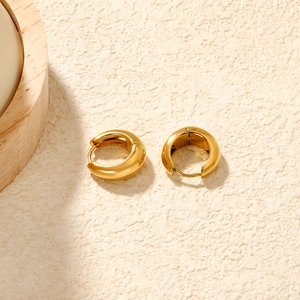 Macro shot of thick high-polished 18K gold plated hoop earrings on textured surface