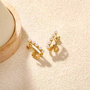 Close-up of gold C-shaped earrings with white pearls and sparkling zircon pavé