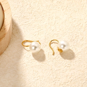 Detailed view of long C-shape gold pearl earrings on a minimalist textured background