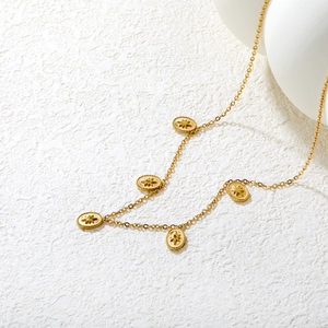 Gros plan du collier doré avec pendentifs ovales gravés d'étoiles sur fond blanc minimaliste