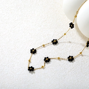 Détail du collier à chaîne dorée avec des breloques fleurs noires et des perles rondes