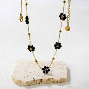 Détail d'un collier doré orné de fleurs noires avec fermoir mousqueton et chaînette