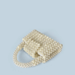 Detail view of handmade pearl handbag with beaded ring handle and zipper on blue backdrop
