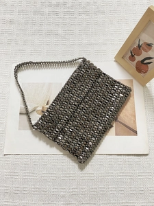 Detailed view of woven gunmetal beads on a metallic evening bag over a textured fabric