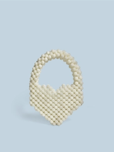 Minimalist beige heart-shaped beaded woven handbag with single handle against blue backdrop