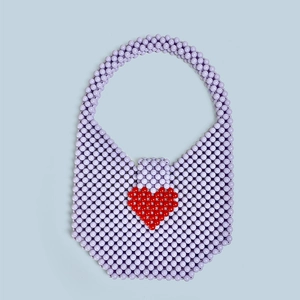 Detail of handmade lilac acrylic beaded bag with a red heart pattern on blue background