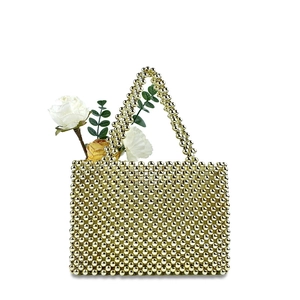 Detail of gold beaded handbag with dual handles and floral decor on white background