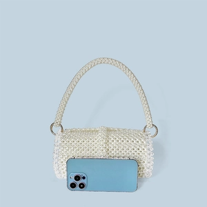 Detail of handcrafted pearl beaded cylinder evening bag next to a smartphone