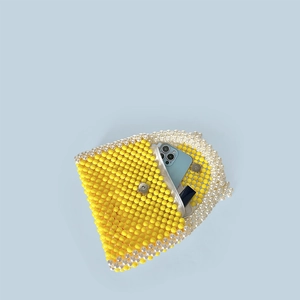 Detailed interior of yellow woven bead handbag showing capacity with phone and lipstick