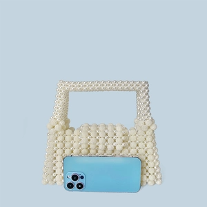 Size comparison of white beaded pearl handbag with smartphone on blue background
