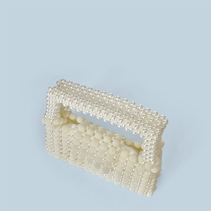 Detail of handmade beaded pearl handbag with woven texture and top handle in off-white